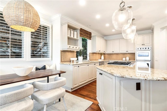 kitchen featuring white double oven, stainless steel gas cooktop, a kitchen island with sink, decorative light fixtures, and white cabinets