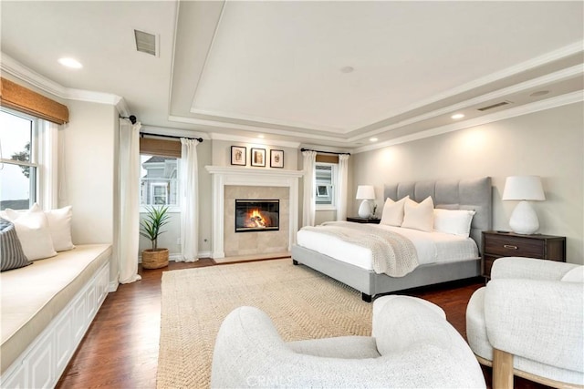 bedroom with a tile fireplace, dark hardwood / wood-style floors, a raised ceiling, and multiple windows