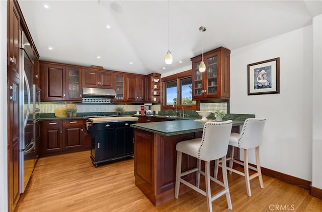 kitchen featuring dark countertops, a peninsula, a sink, under cabinet range hood, and backsplash