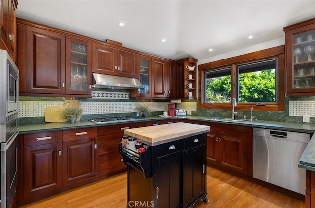 kitchen with under cabinet range hood, stainless steel appliances, butcher block countertops, a sink, and light wood finished floors