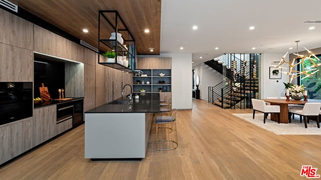 kitchen featuring an island with sink, hanging light fixtures, oven, a breakfast bar area, and light hardwood / wood-style floors