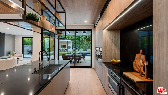 kitchen with stainless steel oven, light hardwood / wood-style floors, sink, and dark stone countertops