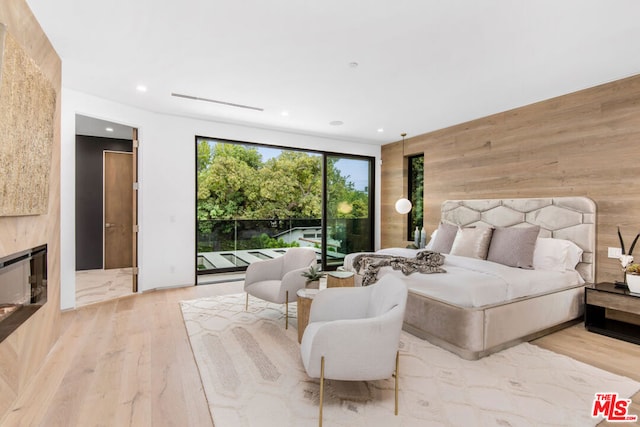 bedroom featuring wood walls, access to outside, a high end fireplace, and light wood-type flooring