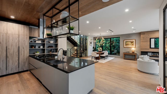 kitchen featuring black gas cooktop, sink, light hardwood / wood-style floors, kitchen peninsula, and pendant lighting