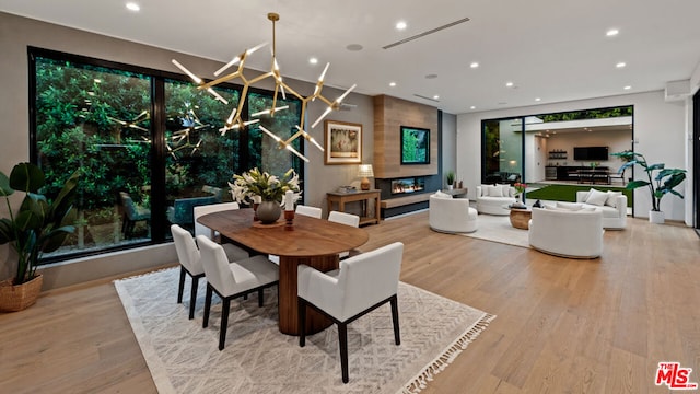 dining area featuring light wood-type flooring, a chandelier, and a large fireplace