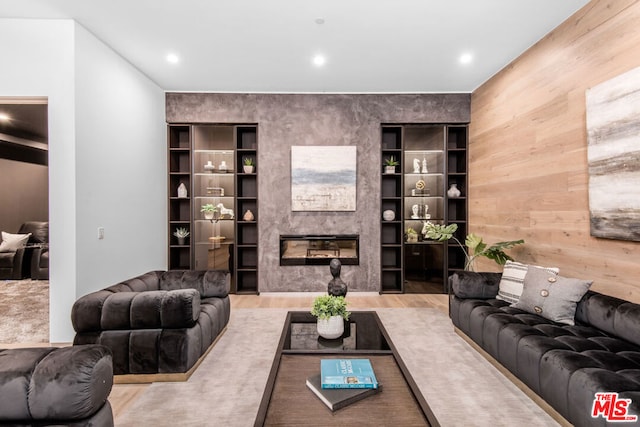 living room featuring light hardwood / wood-style flooring, wood walls, and a large fireplace