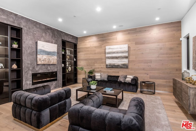 living room with built in shelves, wooden walls, light hardwood / wood-style flooring, and a high end fireplace