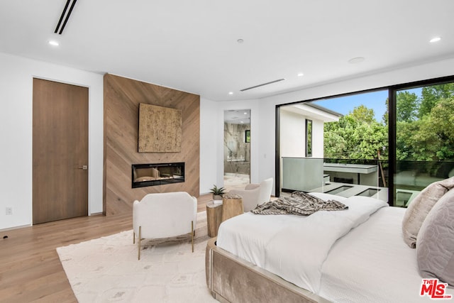 bedroom featuring light wood-type flooring, a fireplace, and connected bathroom