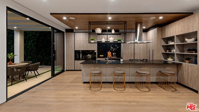 kitchen with sink, kitchen peninsula, wall chimney exhaust hood, a breakfast bar area, and light hardwood / wood-style floors