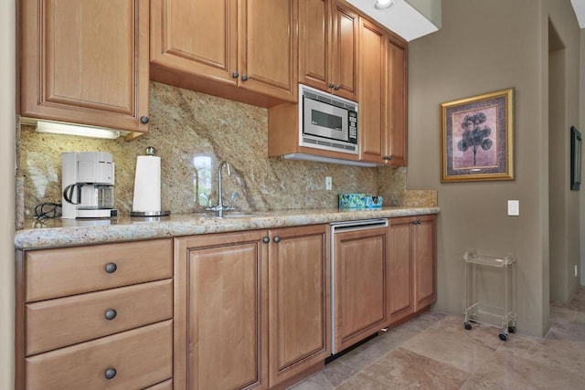 kitchen featuring stainless steel microwave, light stone countertops, sink, and tasteful backsplash