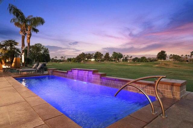 pool at dusk featuring pool water feature and a yard