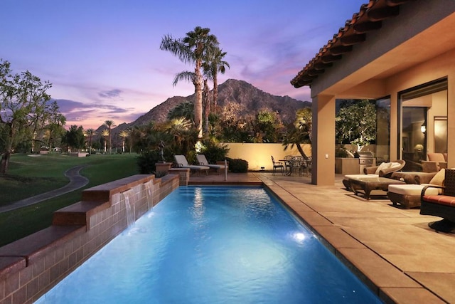 pool at dusk featuring outdoor lounge area, exterior kitchen, a mountain view, pool water feature, and a patio area