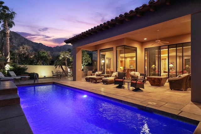 pool at dusk featuring a patio area, ceiling fan, a mountain view, and an outdoor hangout area