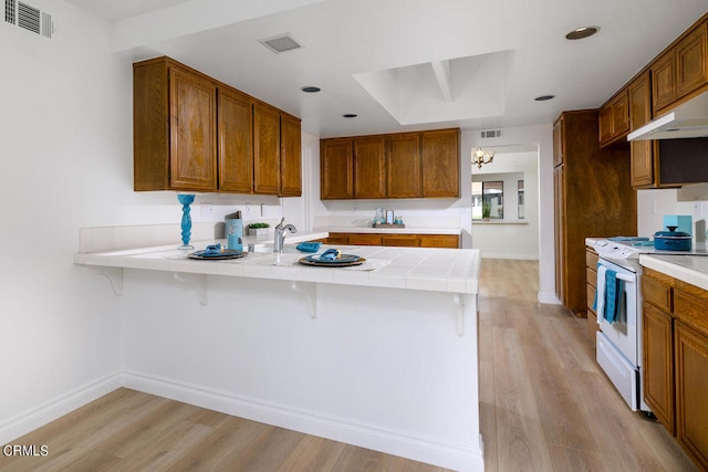 kitchen with kitchen peninsula, white electric stove, light hardwood / wood-style floors, and a breakfast bar