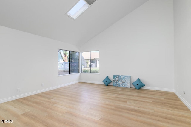 unfurnished room with a skylight, light wood-type flooring, and high vaulted ceiling