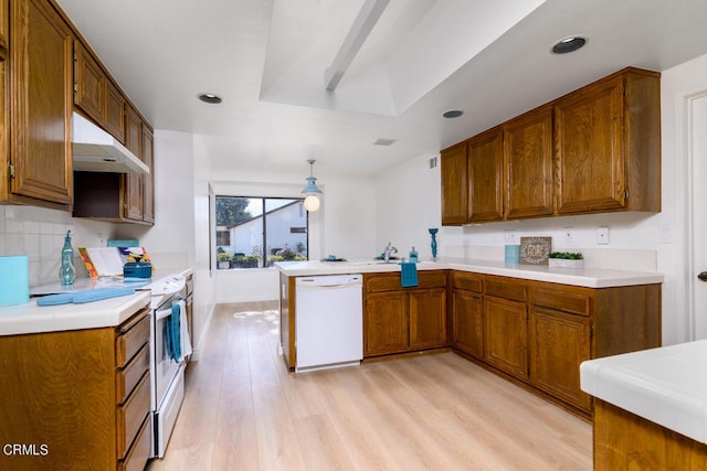 kitchen with white appliances, kitchen peninsula, light hardwood / wood-style flooring, decorative light fixtures, and backsplash