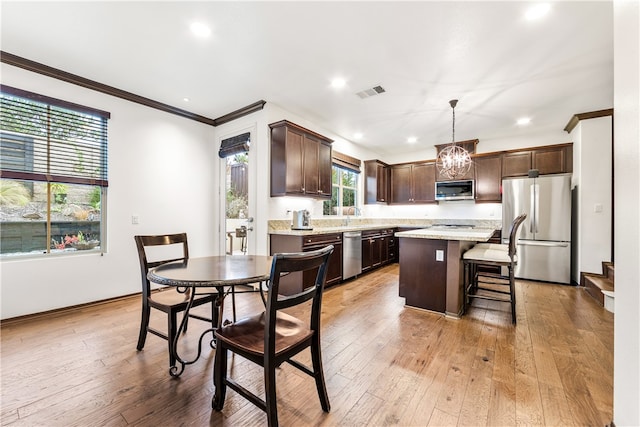 kitchen with light wood-type flooring, ornamental molding, stainless steel appliances, pendant lighting, and a center island