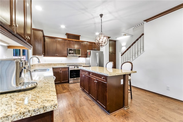 kitchen featuring a kitchen island, a breakfast bar area, light hardwood / wood-style flooring, decorative light fixtures, and appliances with stainless steel finishes