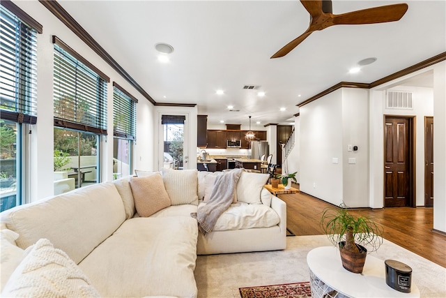 living room with light hardwood / wood-style floors, ornamental molding, and ceiling fan