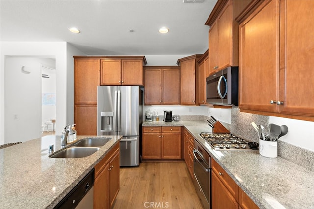 kitchen with sink, light stone counters, decorative backsplash, appliances with stainless steel finishes, and light wood-type flooring