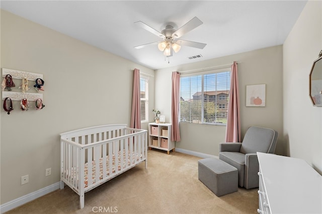 bedroom featuring ceiling fan, light carpet, and a crib