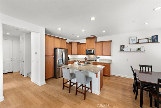 kitchen with light stone countertops, sink, stainless steel appliances, a kitchen breakfast bar, and a kitchen island with sink