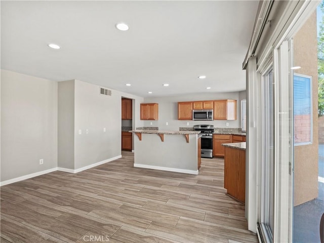 kitchen featuring a breakfast bar area, visible vents, appliances with stainless steel finishes, a center island, and brown cabinetry