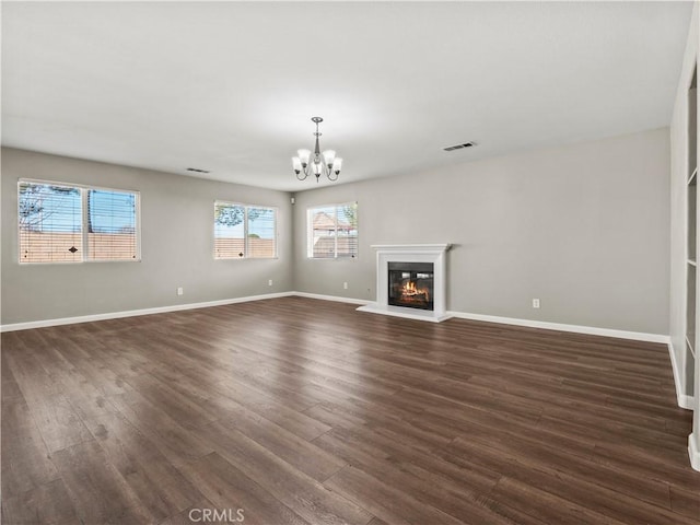 unfurnished living room featuring dark wood-style floors, visible vents, a notable chandelier, and a glass covered fireplace