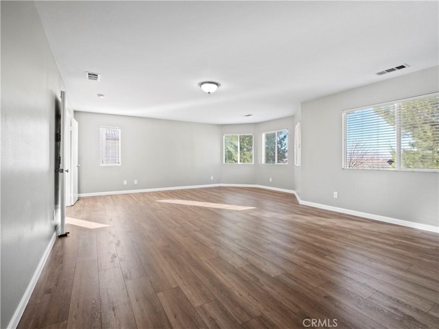 unfurnished room featuring dark wood finished floors, visible vents, and baseboards