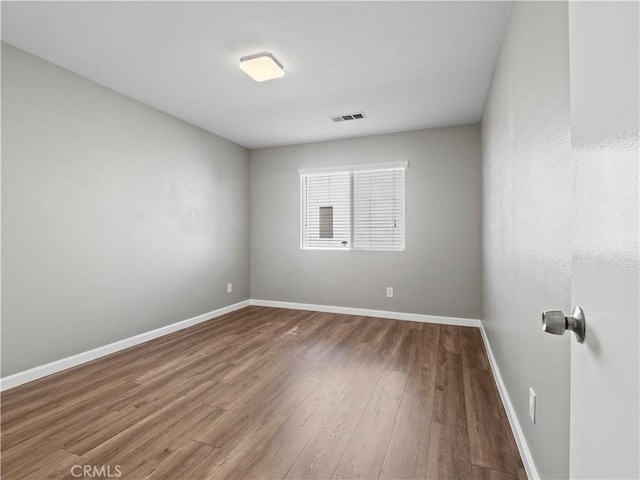 empty room featuring wood finished floors, visible vents, and baseboards