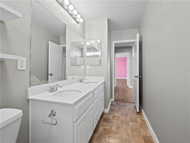 bathroom with toilet, a sink, baseboards, and double vanity