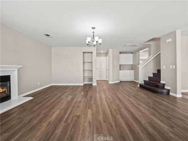 unfurnished living room featuring dark wood-style flooring, stairway, a glass covered fireplace, and visible vents