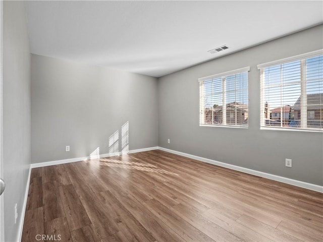 empty room featuring visible vents, baseboards, and wood finished floors