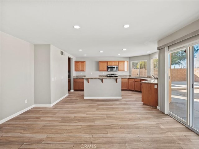 kitchen with recessed lighting, stainless steel appliances, brown cabinets, wood tiled floor, and a kitchen bar