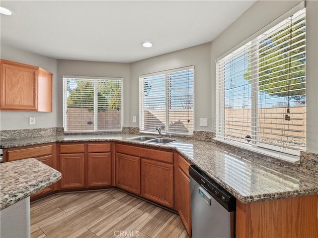 kitchen with light wood finished floors, dishwasher, brown cabinets, stone counters, and a sink