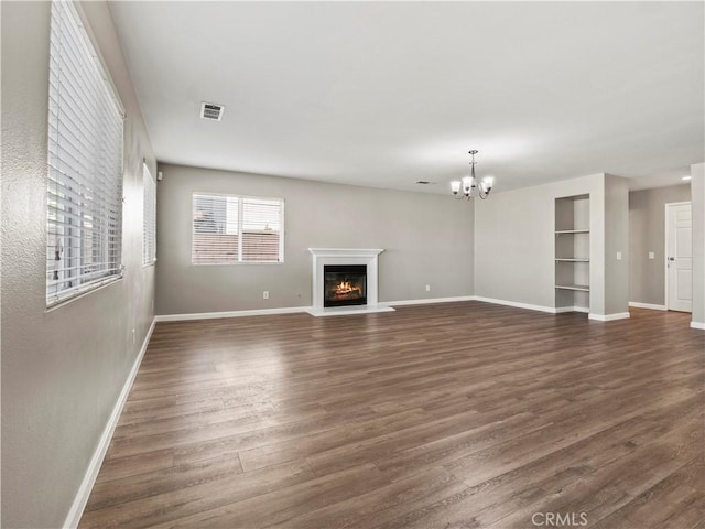 unfurnished living room with a notable chandelier, baseboards, dark wood-style flooring, and a glass covered fireplace