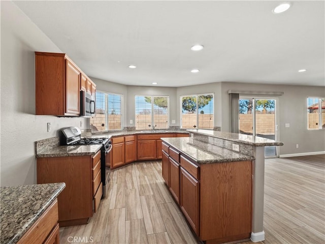 kitchen featuring brown cabinets, stainless steel appliances, recessed lighting, light wood-style flooring, and stone countertops