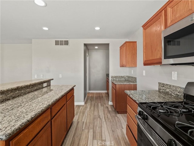 kitchen featuring visible vents, stainless steel microwave, gas range, and light stone countertops