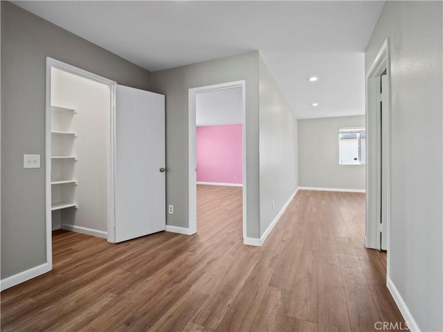 interior space featuring baseboards, a walk in closet, wood finished floors, and recessed lighting