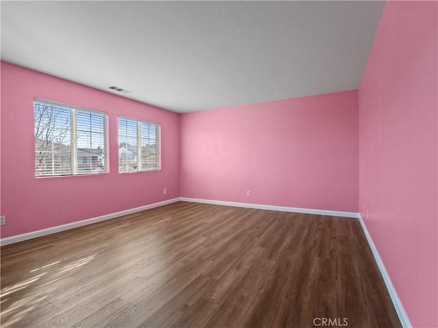 empty room featuring baseboards, visible vents, and wood finished floors