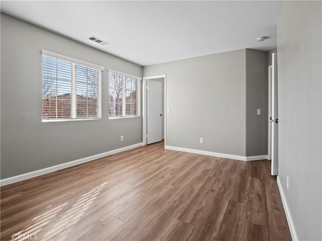 unfurnished room featuring visible vents, baseboards, and wood finished floors