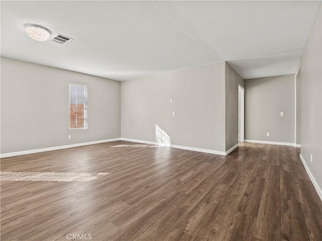 unfurnished room featuring visible vents, dark wood finished floors, and baseboards