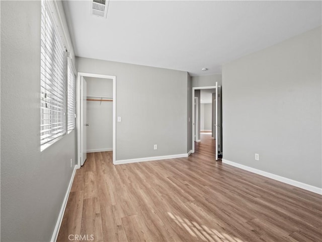 unfurnished bedroom featuring visible vents, baseboards, a closet, light wood-type flooring, and a walk in closet