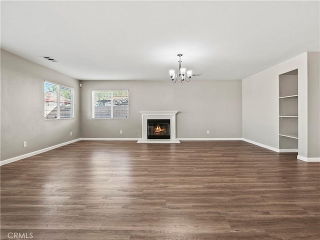 unfurnished living room featuring baseboards, visible vents, a glass covered fireplace, dark wood-type flooring, and a chandelier