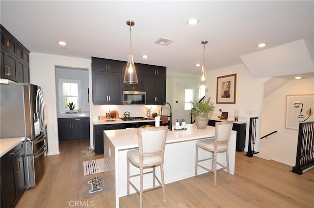 kitchen featuring stainless steel appliances, a kitchen breakfast bar, an island with sink, decorative light fixtures, and light wood-type flooring