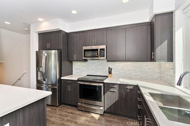 kitchen with dark brown cabinetry, sink, tasteful backsplash, dark wood-type flooring, and appliances with stainless steel finishes