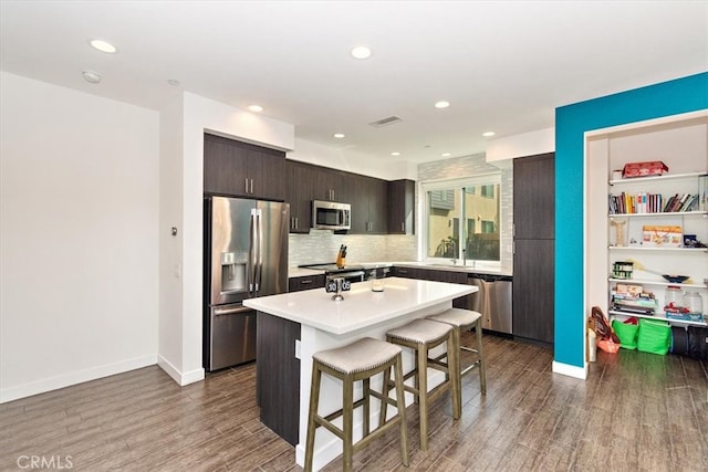 kitchen with a kitchen island, dark hardwood / wood-style flooring, stainless steel appliances, and a breakfast bar