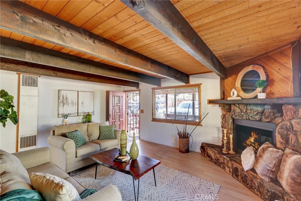 living room featuring a stone fireplace, beam ceiling, wooden ceiling, and light wood-type flooring