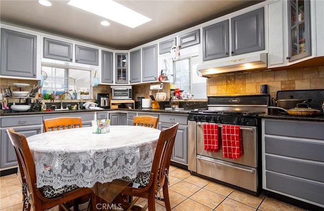 kitchen featuring gas range, gray cabinets, light tile patterned floors, and tasteful backsplash