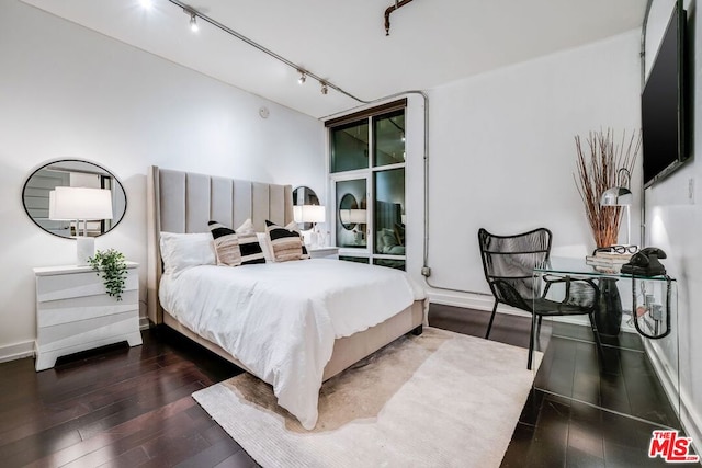 bedroom with dark hardwood / wood-style flooring and track lighting